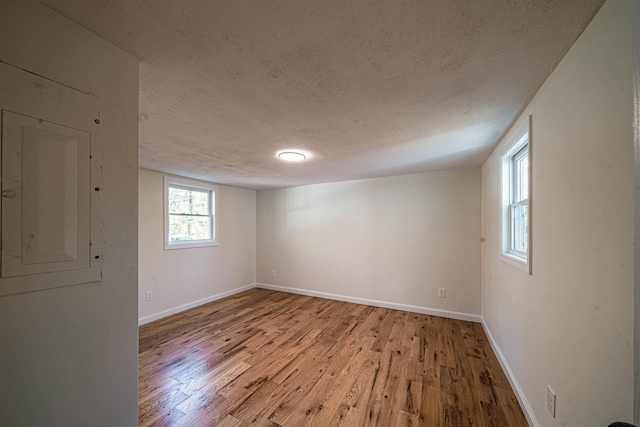 empty room with baseboards, a textured ceiling, wood finished floors, and electric panel