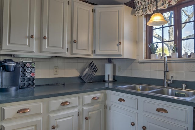 kitchen with white cabinets, backsplash, dark countertops, and a sink