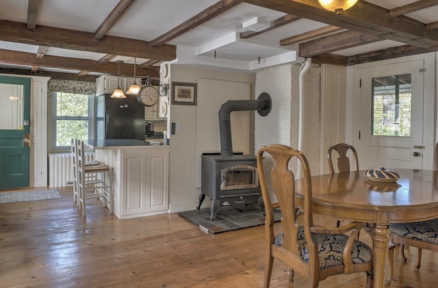 dining space featuring a wood stove, light wood finished floors, and beamed ceiling