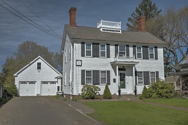 colonial home featuring a detached garage, a chimney, an outdoor structure, and a front lawn