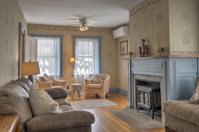 living room with wood finished floors, baseboards, a wall mounted air conditioner, wallpapered walls, and a ceiling fan