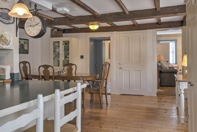 dining area featuring beamed ceiling and light wood-style flooring