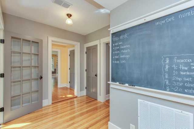 corridor with baseboards, wood finished floors, and visible vents