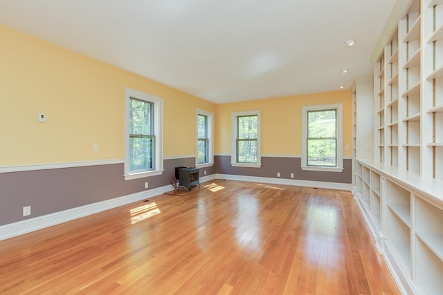 unfurnished living room with light wood-type flooring, a wood stove, baseboards, and a wealth of natural light