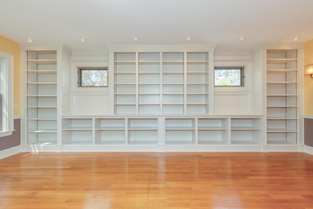 unfurnished living room featuring light wood-style floors, built in features, crown molding, and baseboards