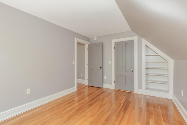 bonus room featuring built in features, baseboards, vaulted ceiling, and light wood-type flooring
