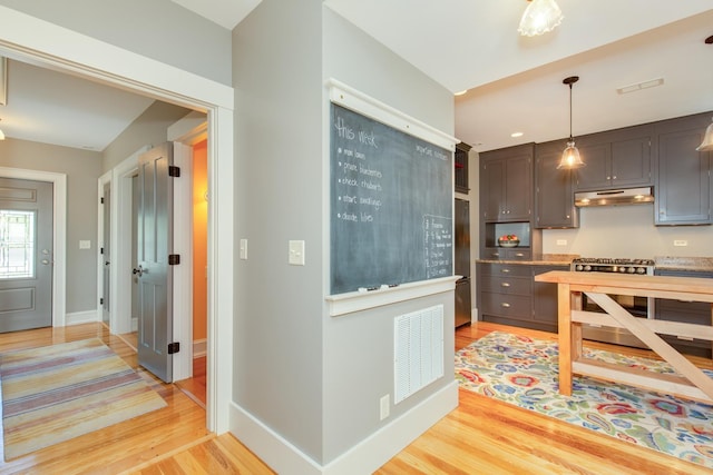 kitchen with stainless steel gas range, hanging light fixtures, light wood-type flooring, under cabinet range hood, and visible vents