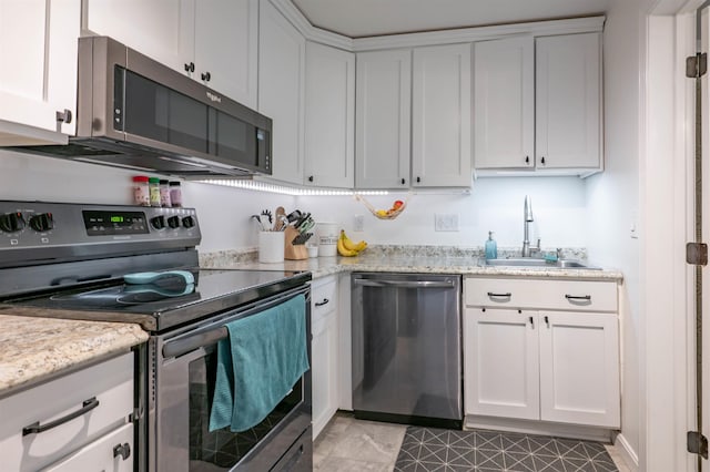 kitchen with light stone counters, a sink, white cabinetry, and stainless steel appliances