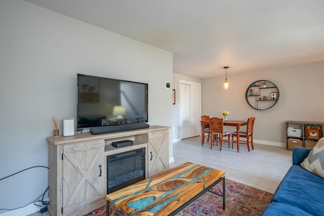 living area featuring baseboards, light wood finished floors, and a glass covered fireplace