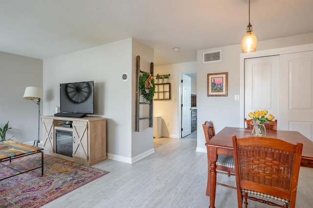 dining room featuring visible vents, baseboards, a glass covered fireplace, and light wood-type flooring