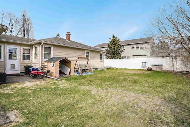 back of property featuring fence, a storage unit, an outbuilding, a chimney, and a yard