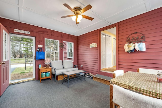 carpeted living room featuring a ceiling fan and wood walls