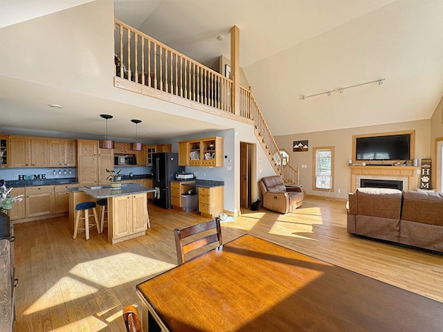 dining space featuring track lighting, stairs, a fireplace, high vaulted ceiling, and light wood-style flooring