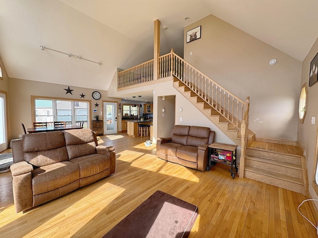 living room featuring rail lighting, high vaulted ceiling, hardwood / wood-style flooring, and stairway