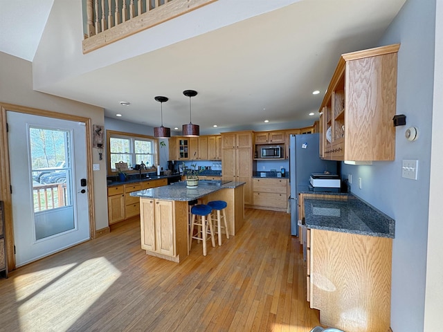 kitchen featuring a kitchen breakfast bar, a sink, stainless steel microwave, recessed lighting, and light wood-style flooring