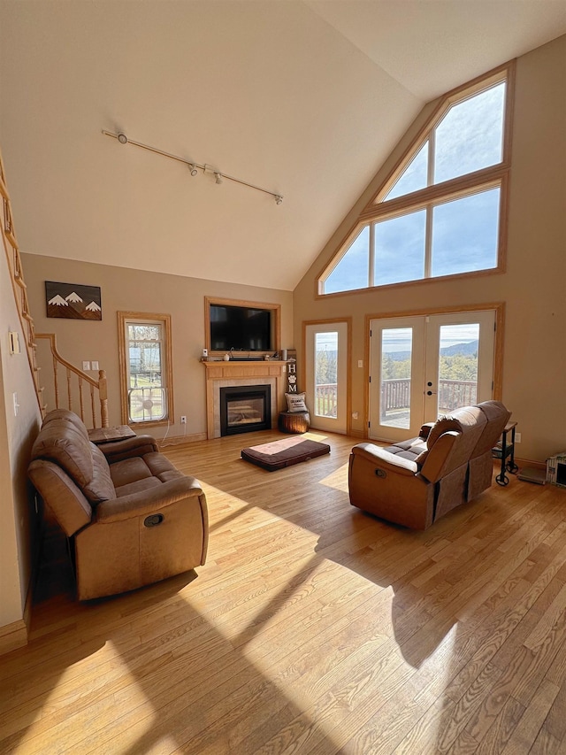 living room featuring track lighting, a glass covered fireplace, wood finished floors, and high vaulted ceiling