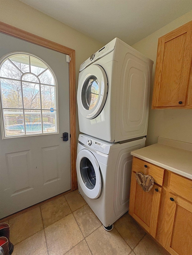 laundry room featuring stacked washing maching and dryer, light tile patterned floors, and cabinet space