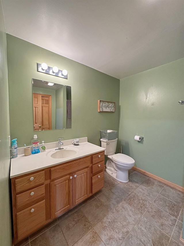 bathroom featuring toilet, baseboards, stone finish floor, and vanity