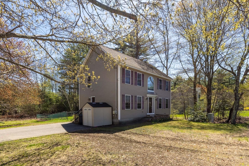 view of property exterior with driveway, a lawn, fence, an outdoor structure, and a storage unit