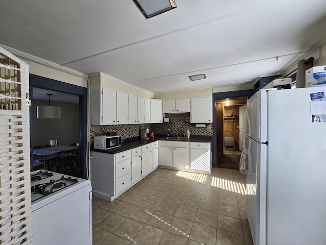 kitchen with dark countertops, a sink, tile patterned floors, white appliances, and white cabinetry
