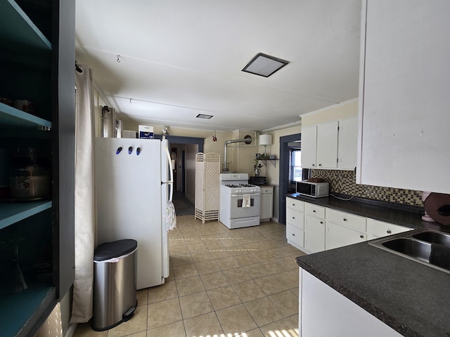 kitchen with dark countertops, a sink, light tile patterned floors, white cabinets, and white appliances