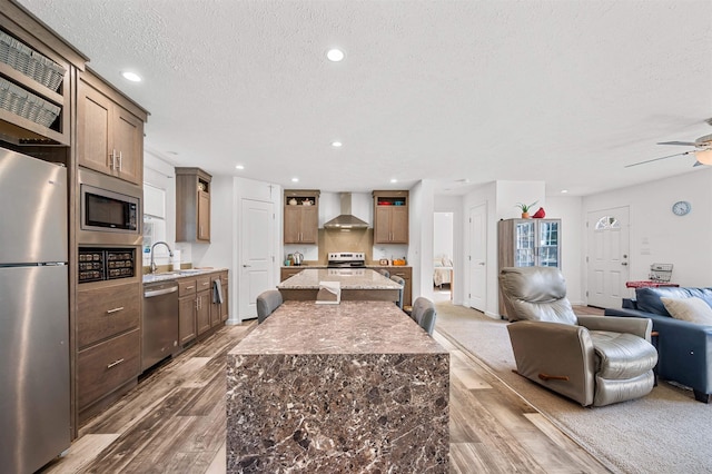 kitchen featuring a center island, wood finished floors, open floor plan, stainless steel appliances, and wall chimney exhaust hood