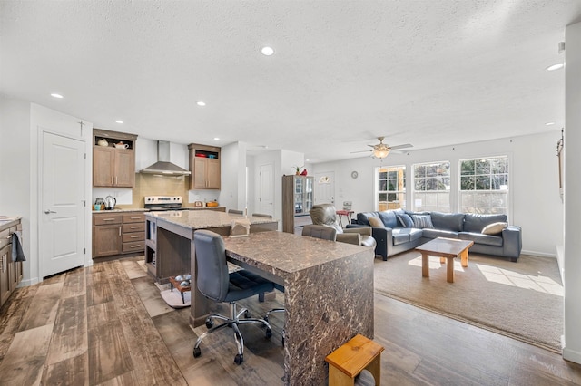 kitchen featuring wall chimney range hood, a textured ceiling, ceiling fan, and wood finished floors