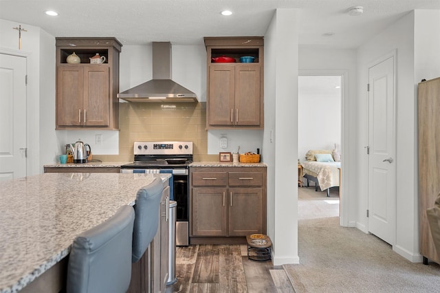 kitchen featuring decorative backsplash, wall chimney range hood, recessed lighting, light stone counters, and stainless steel electric range oven