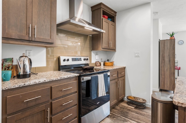 kitchen with wall chimney range hood, decorative backsplash, electric range, light stone countertops, and dark wood-style floors