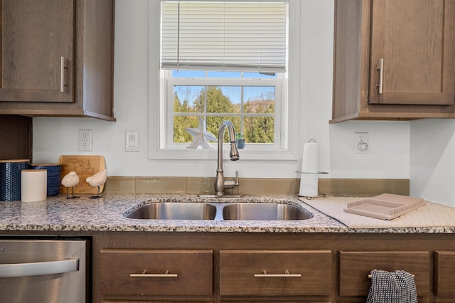 kitchen with light stone counters, a sink, and dishwasher
