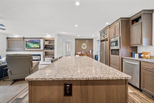 kitchen with appliances with stainless steel finishes, a center island, light stone counters, open floor plan, and light wood-style flooring