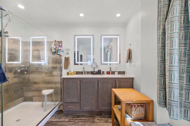full bath featuring crown molding, a sink, double vanity, wood finished floors, and a stall shower