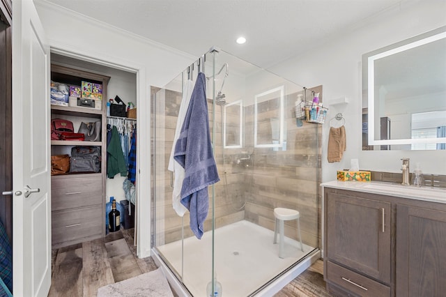 bathroom with a walk in closet, vanity, a shower stall, wood finished floors, and ornamental molding