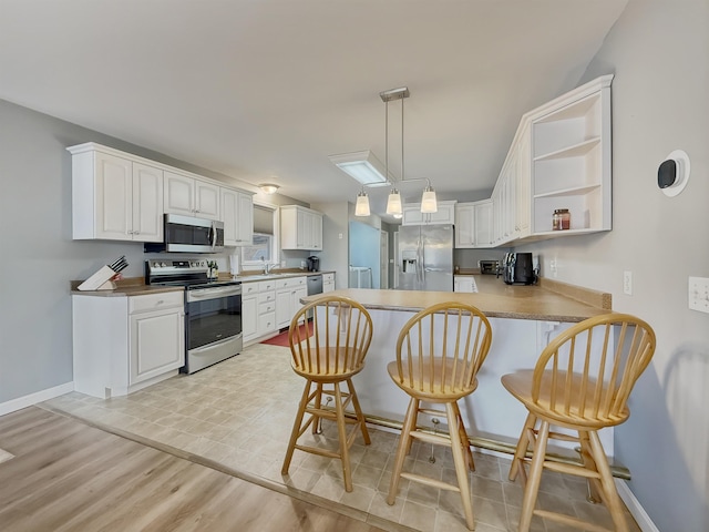 kitchen featuring open shelves, baseboards, a peninsula, a breakfast bar, and stainless steel appliances