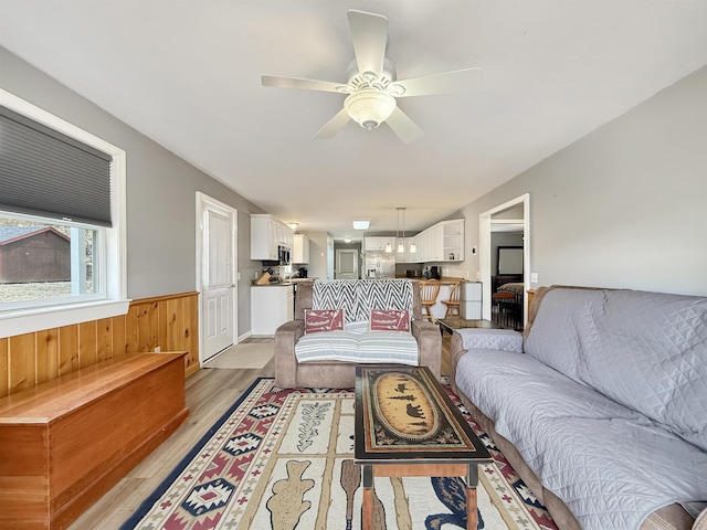 living area with light wood-style flooring, ceiling fan, a wainscoted wall, and wooden walls