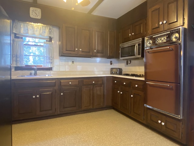 kitchen with double oven, ceiling fan, light countertops, stainless steel microwave, and a sink