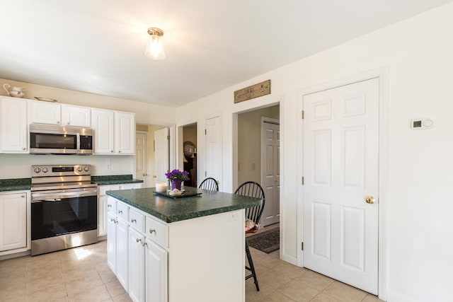 kitchen with a kitchen breakfast bar, dark countertops, appliances with stainless steel finishes, white cabinetry, and light tile patterned flooring
