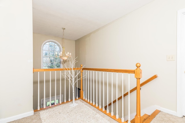 hallway with carpet floors, baseboards, a chandelier, and an upstairs landing