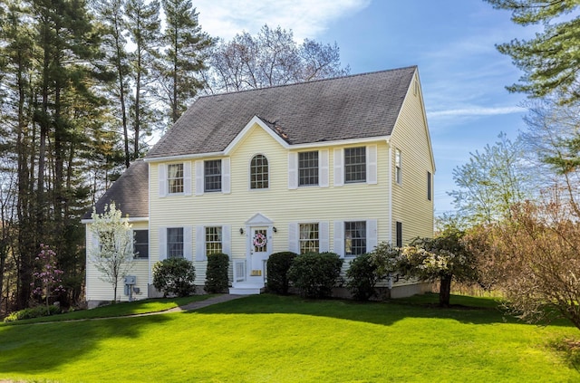 colonial house featuring roof with shingles and a front yard
