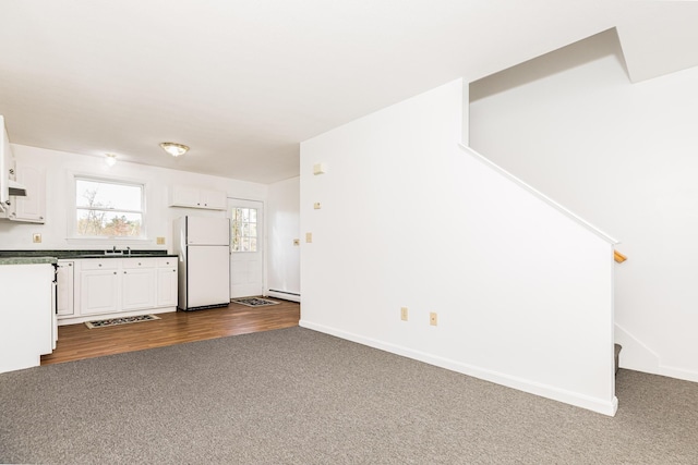 unfurnished living room featuring a sink, baseboards, baseboard heating, and dark carpet