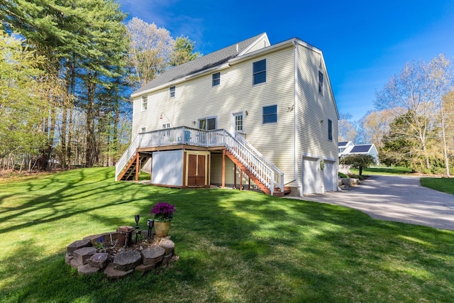 rear view of property featuring a garage, a deck, stairway, a lawn, and driveway
