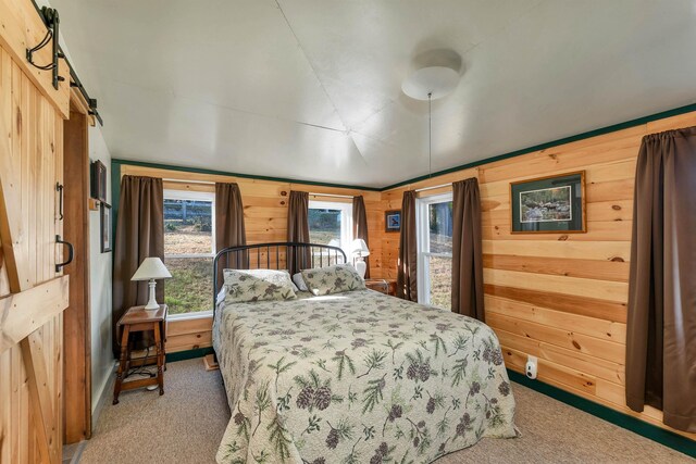carpeted bedroom featuring wood walls and a barn door