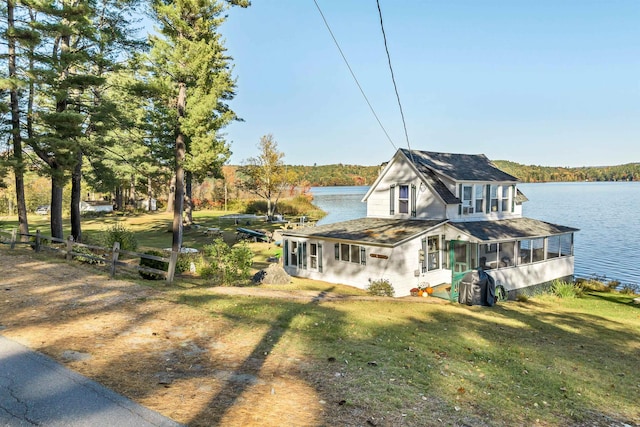 view of front facade featuring fence, a water view, a shingled roof, and a front lawn