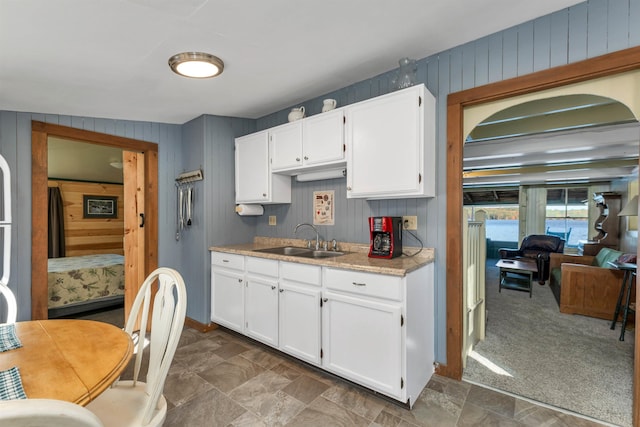 kitchen featuring a sink, light countertops, wood walls, stone finish floor, and white cabinetry