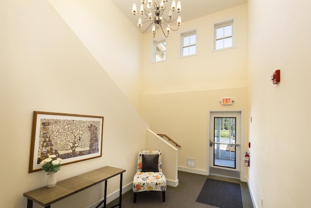 foyer with baseboards, a high ceiling, a notable chandelier, and dark colored carpet