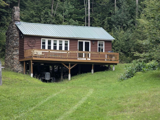 back of property with metal roof, a wooded view, a wooden deck, and faux log siding