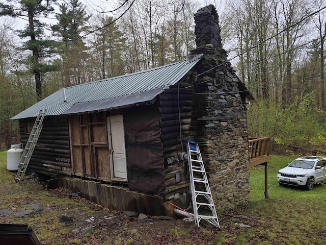 view of property exterior featuring log exterior, a chimney, and metal roof
