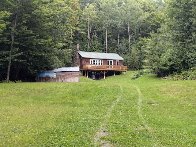 view of front of house featuring a deck, a view of trees, metal roof, a front lawn, and a chimney