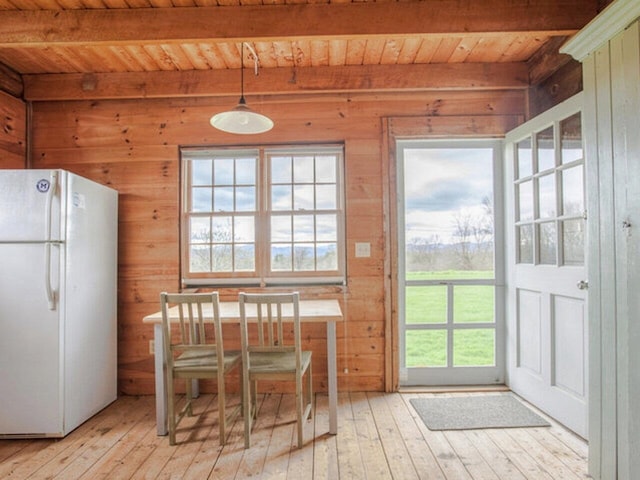 dining space featuring beam ceiling, wood walls, wood ceiling, and light wood finished floors
