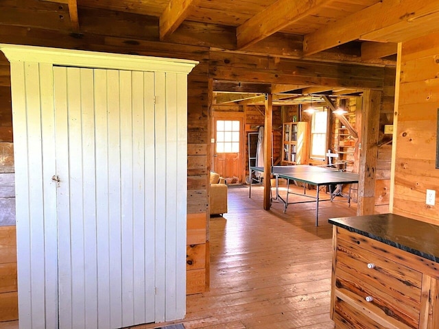 corridor featuring light wood-style flooring, wooden walls, wood ceiling, and beamed ceiling